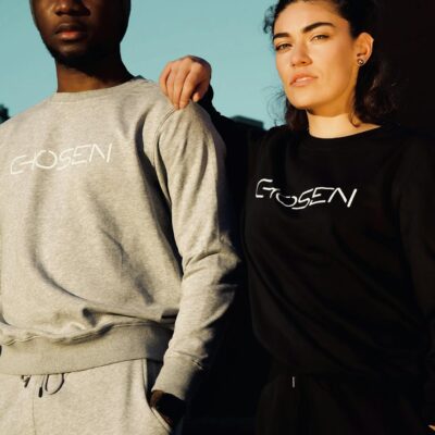 A couple poses in stylish Chosen sweatshirts under bright outdoor daylight.