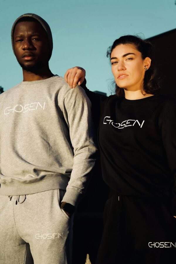 A couple poses in stylish Chosen sweatshirts under bright outdoor daylight.