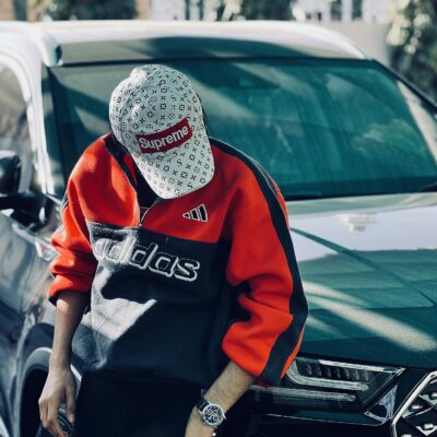 Stylish young man in designer clothing leaning on a luxury car outdoors.