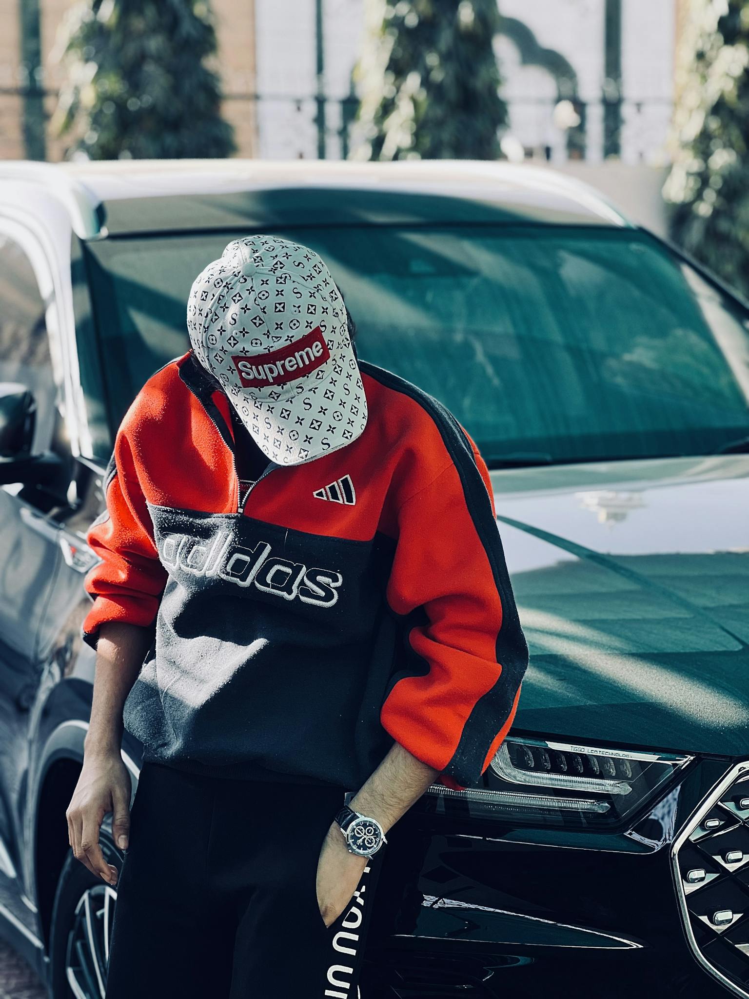 Stylish young man in designer clothing leaning on a luxury car outdoors.